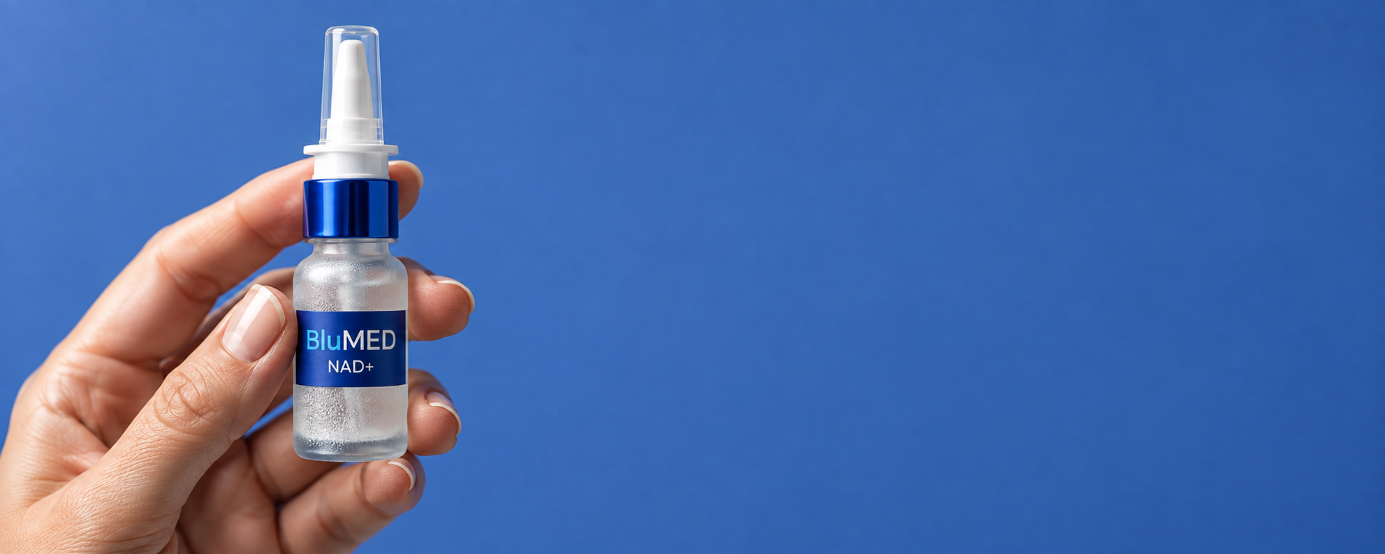 A hand holding a BluMED NAD+ nasal spray bottle against a blue background